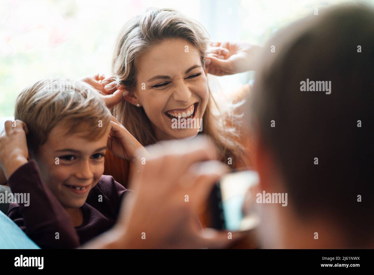 Femme joyeuse avec son fils photographiée par l'homme à la maison Banque D'Images