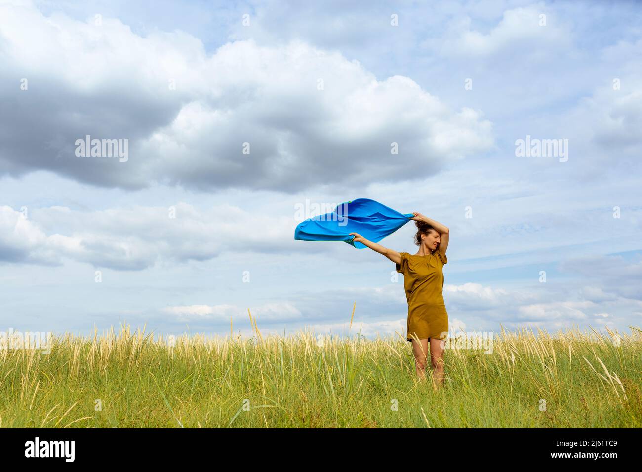 Femme tenant une écharpe bleu en douceur balayée par le vent dans un pré Banque D'Images