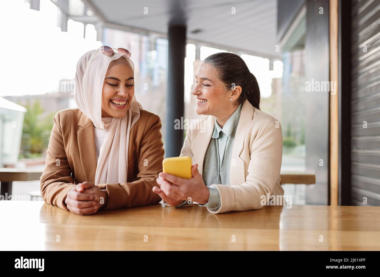 Bonne femme d'affaires partageant un smartphone assis à une table dans un café Banque D'Images