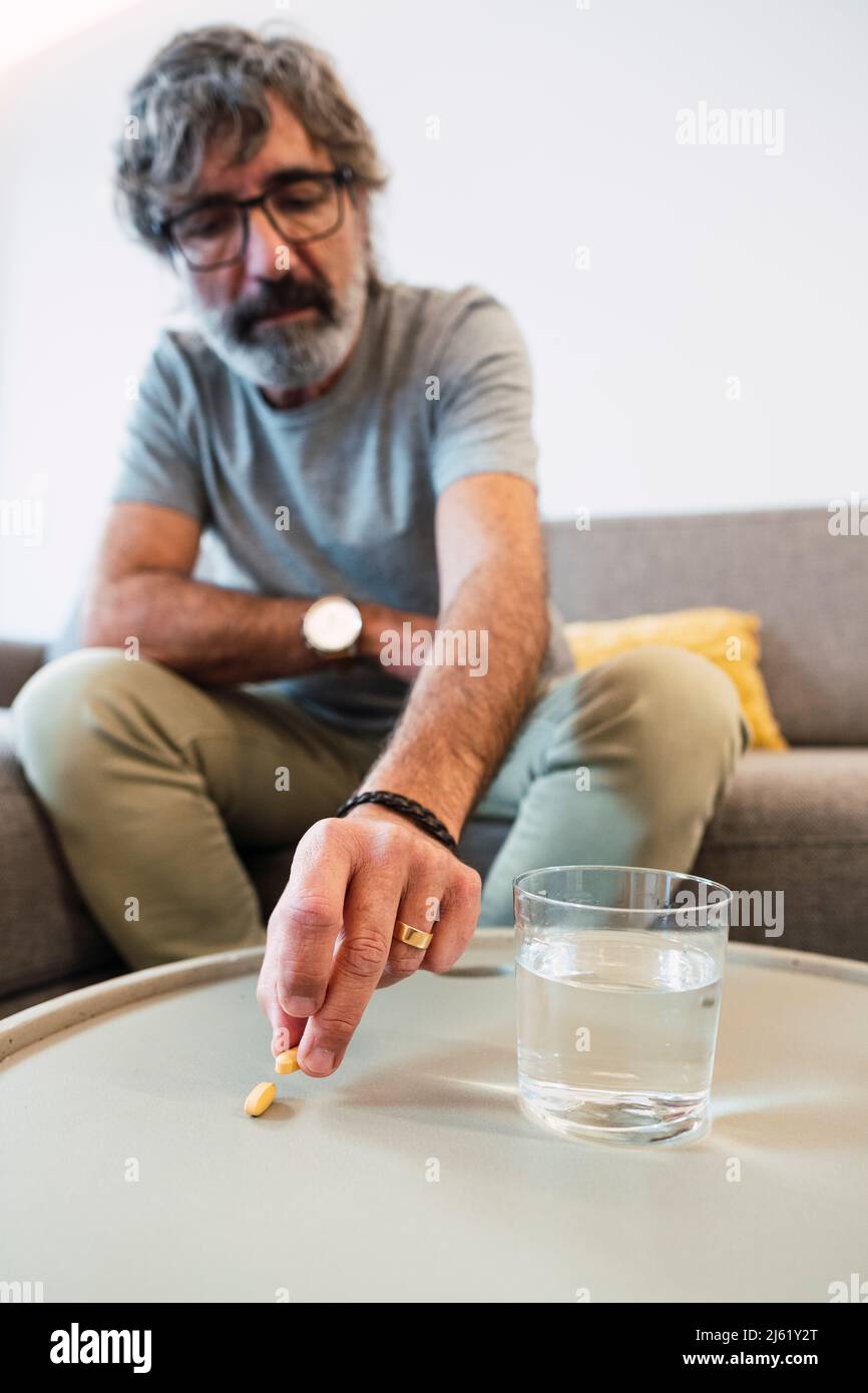 Homme âgé avec un verre d'eau et prenant la pilule de médicaments assis sur le canapé à la maison Banque D'Images