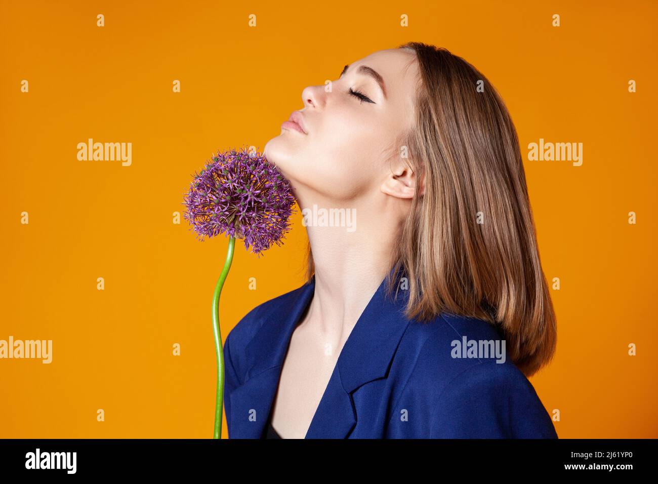 Jeune femme avec les yeux fermés touchant allium sur le menton contre la couleur orange Banque D'Images
