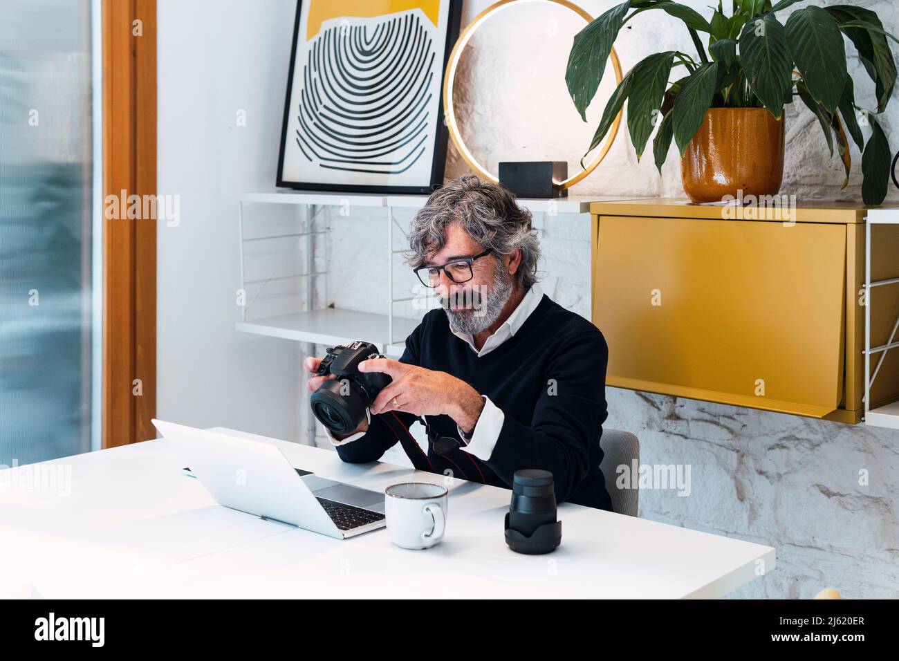 Pigiste souriant tenant la caméra assis avec un ordinateur portable à la table Banque D'Images