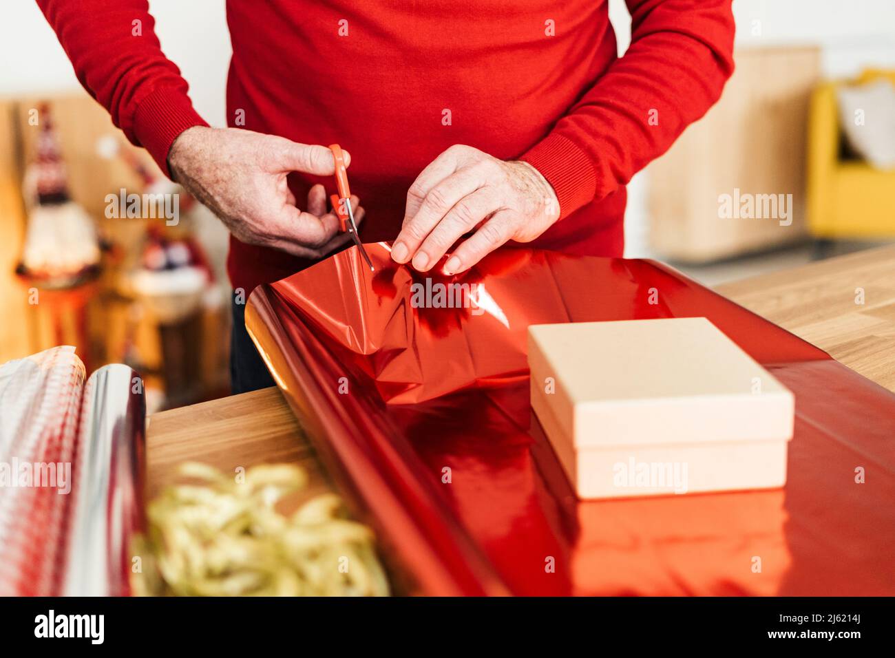Main de l'homme senior emballant le cadeau de Noël sur la table à la maison Banque D'Images