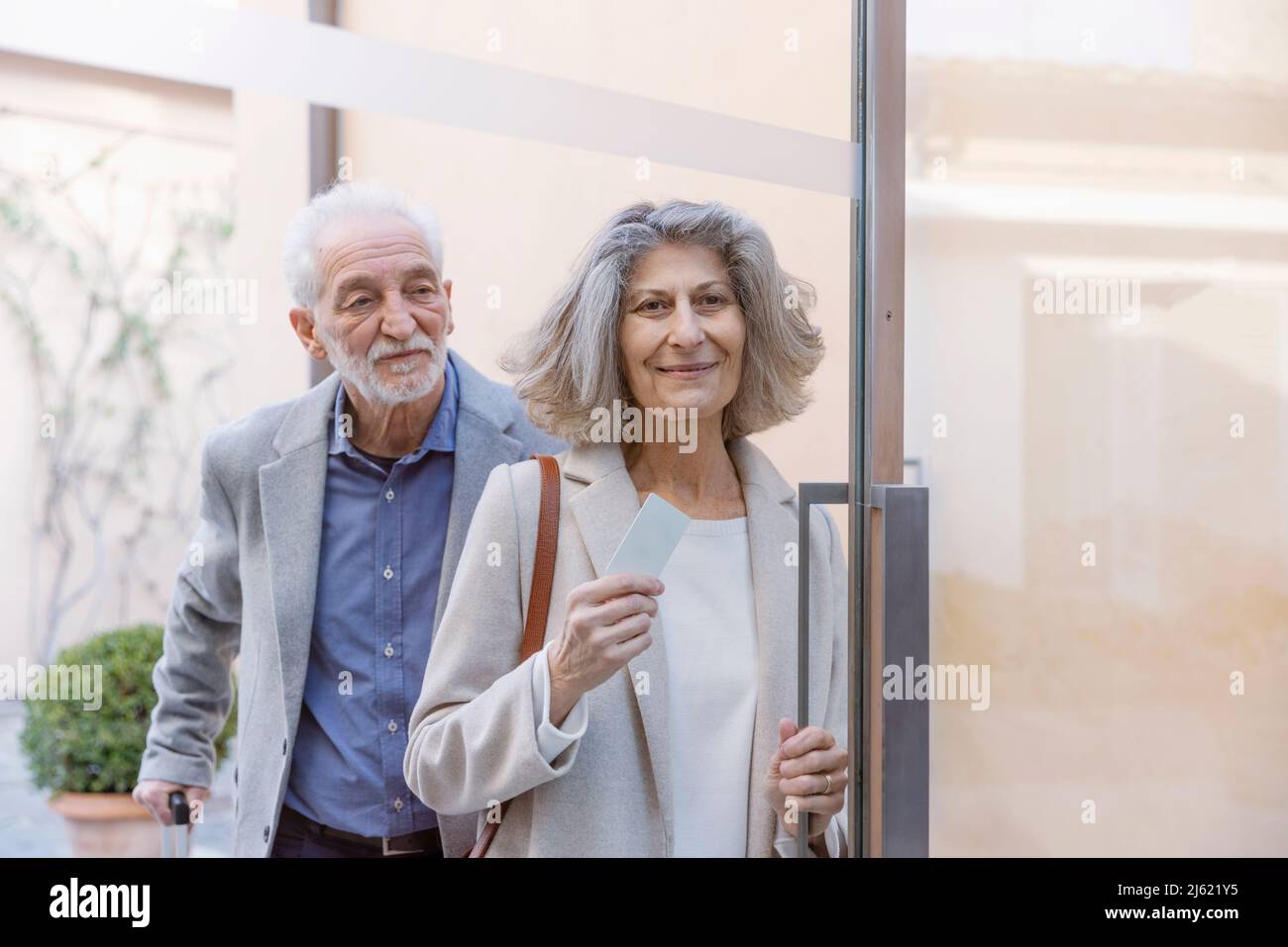 Couple senior avec cardkey debout à la porte vitrée de l'hôtel-boutique Banque D'Images