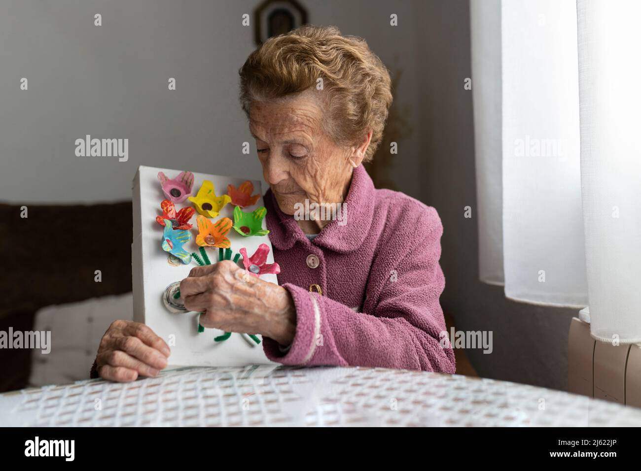 Femme senior décorant des objets en papier assis à la table de salle à manger Banque D'Images