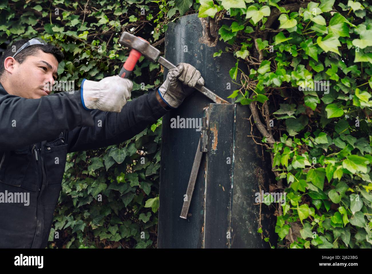 Ouvrier de construction avec marteau travaillant sur la porte en métal Banque D'Images