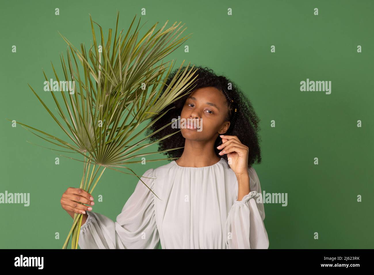 Jeune femme tenant des branches de paume devant un fond vert Banque D'Images