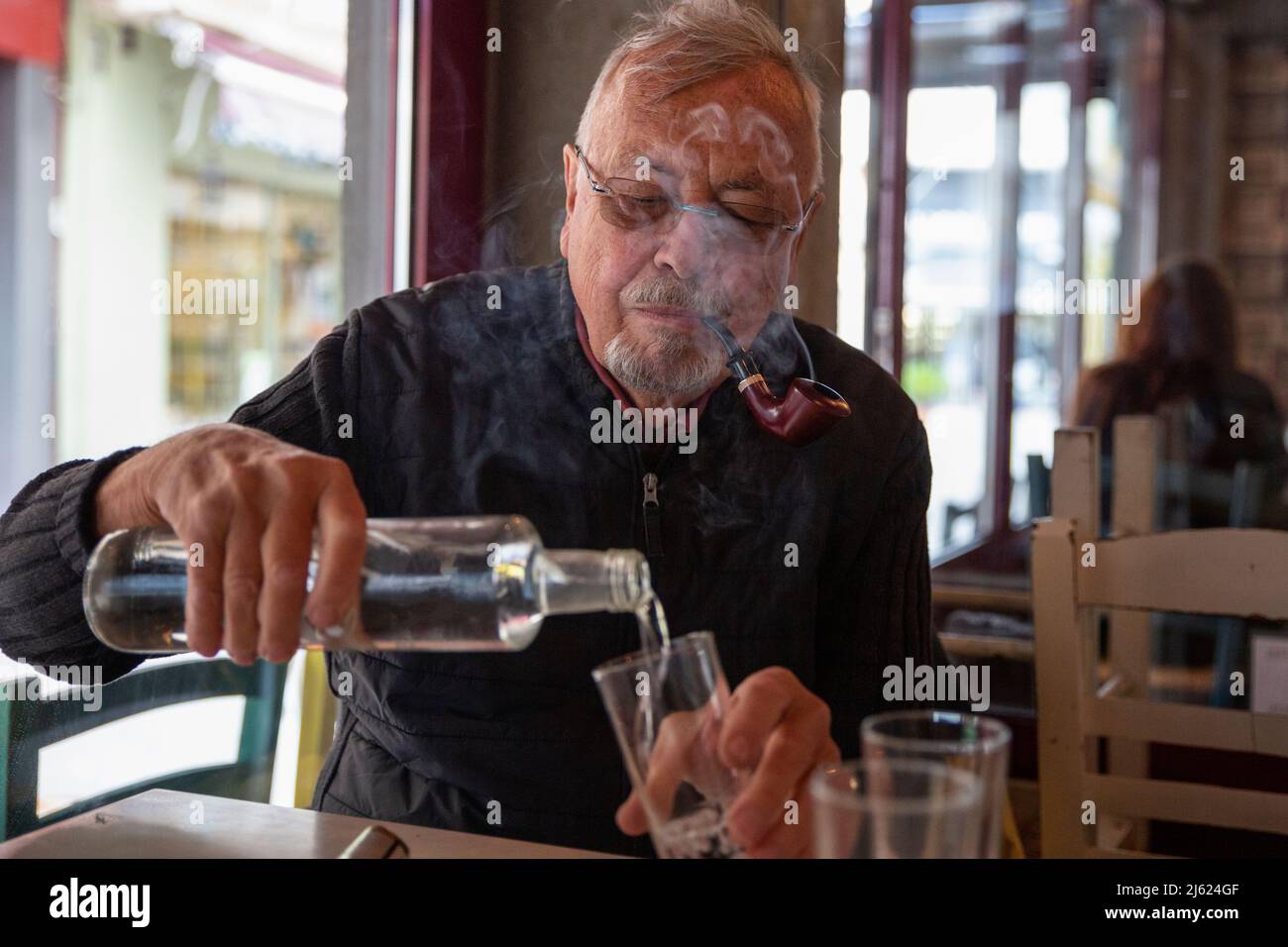 Homme âgé fumant un cigare dans un verre assis à une table Banque D'Images