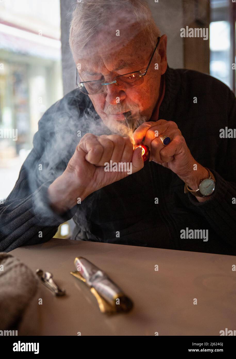 Homme âgé portant des lunettes fumant un cigare assis à une table Banque D'Images