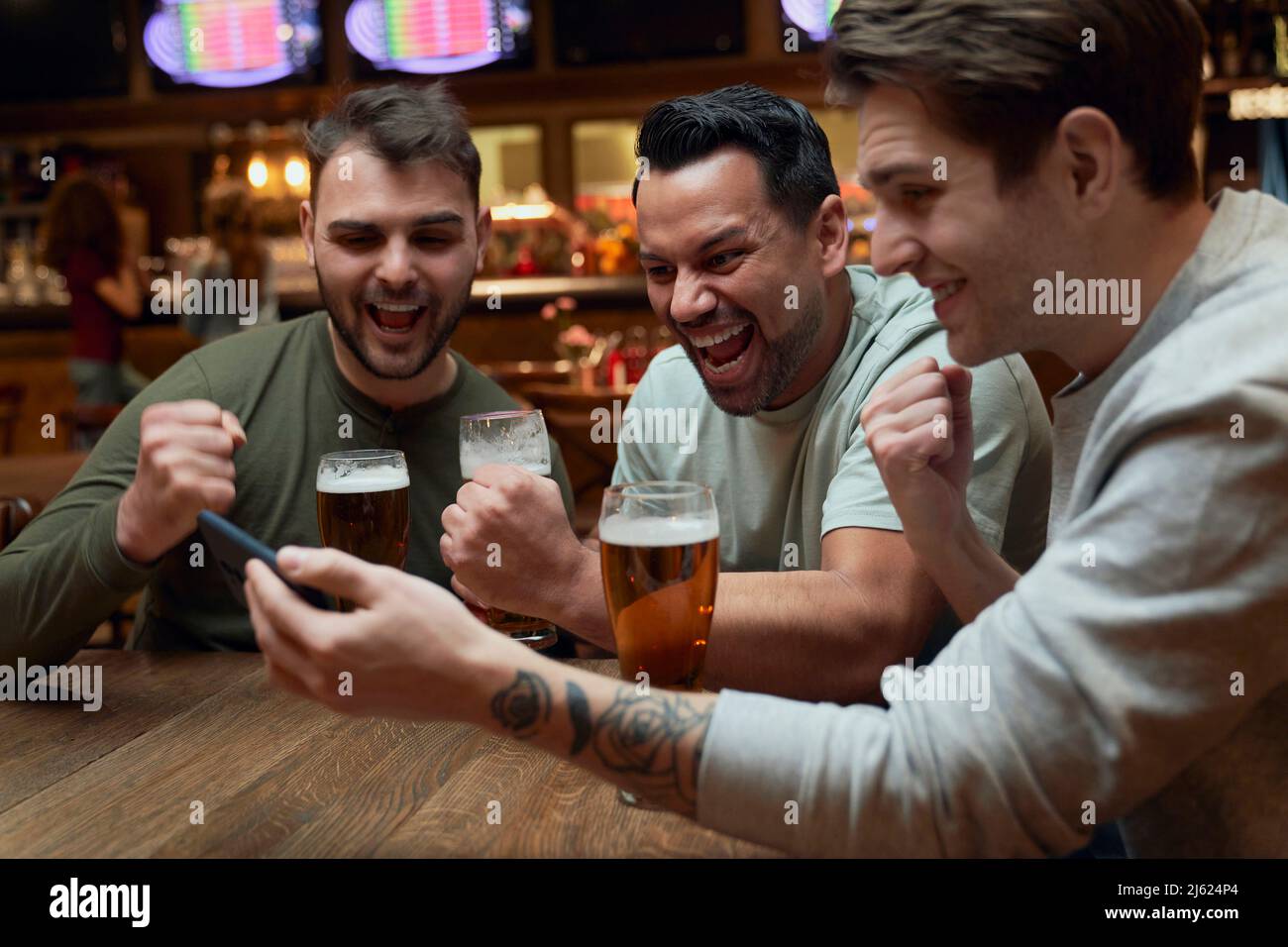 Trois joyeux fans de football masculin ayant de la bière et regardant un match sur smartphone dans un pub Banque D'Images