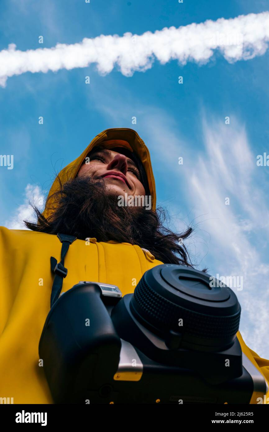 Femme souriante avec caméra debout sous un ciel nuageux Banque D'Images
