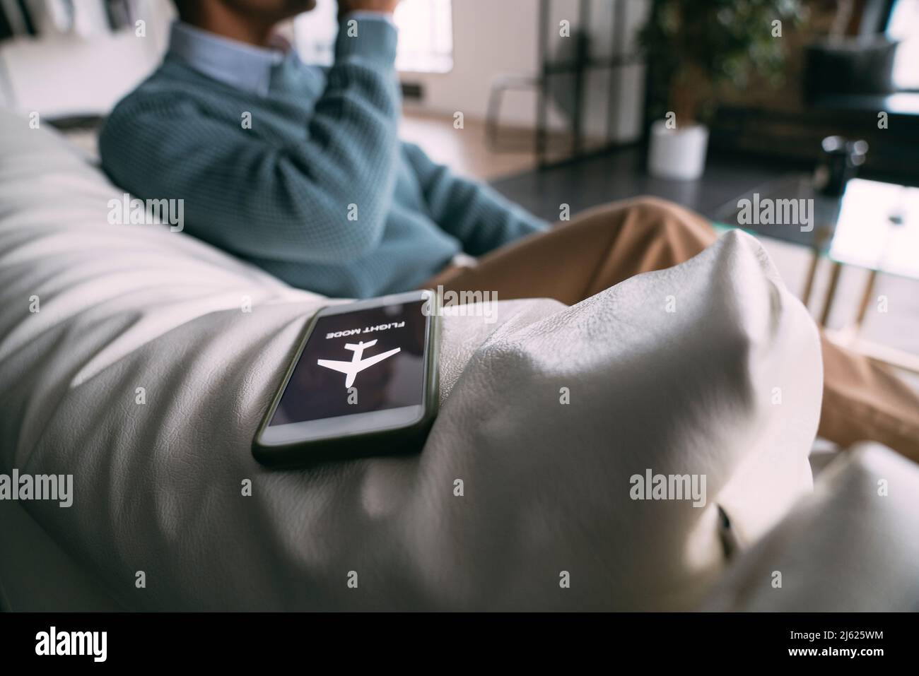 Symbole du mode avion sur le téléphone portable par un homme assis sur le canapé à la maison Banque D'Images
