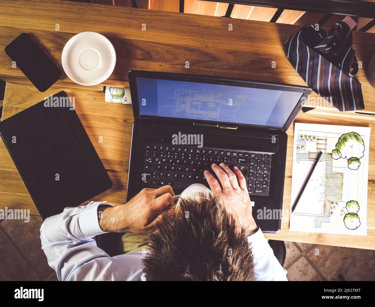 l'image montre un homme qui travaille sur un ordinateur portable au bureau à domicile et qui boit un café tout en écrivant sur un ordinateur portable ou un ordinateur, un bureau en bois et un plan de jardin ou des Banque D'Images