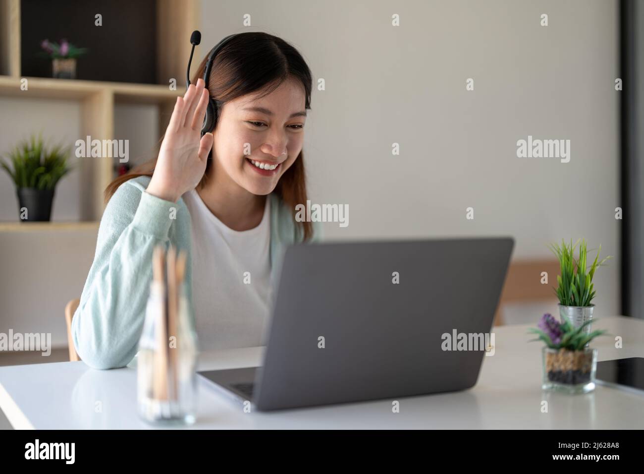 Attrayant heureux jeune étudiant étudiant en ligne à la maison, en utilisant un ordinateur portable, des écouteurs, avoir le chat vidéo, agitant. Travail à distance, enseignement à distance Banque D'Images