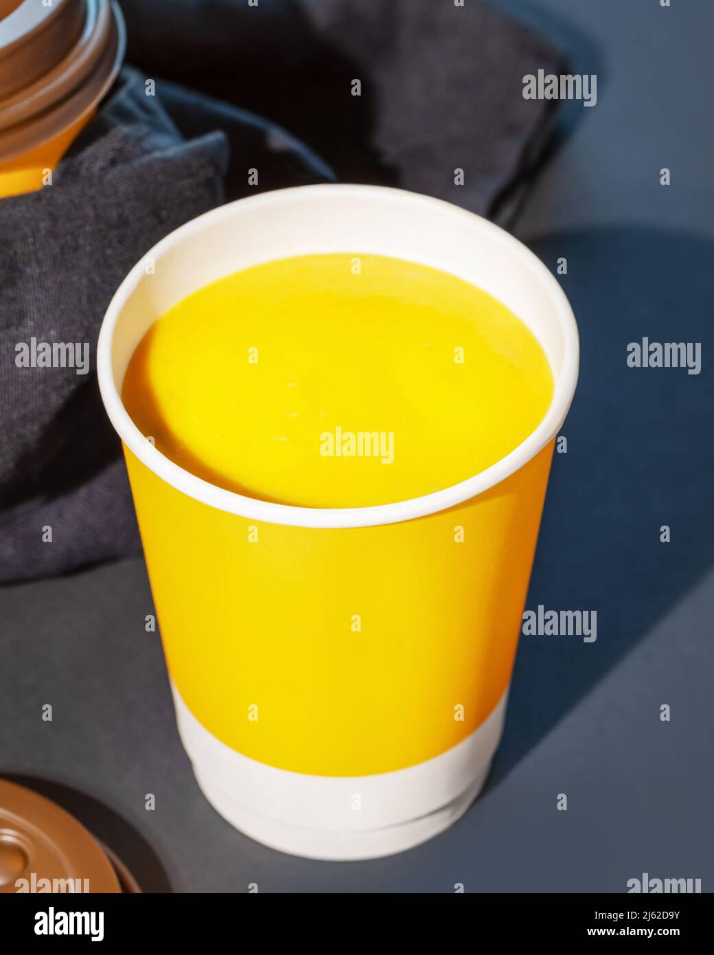 Soupe naturelle épaisse à la crème de citrouille végétalienne avec graines dans une tasse jetable sur fond bleu foncé. Concept de soupe à emporter, de nourriture à emporter et de nourriture saine Banque D'Images
