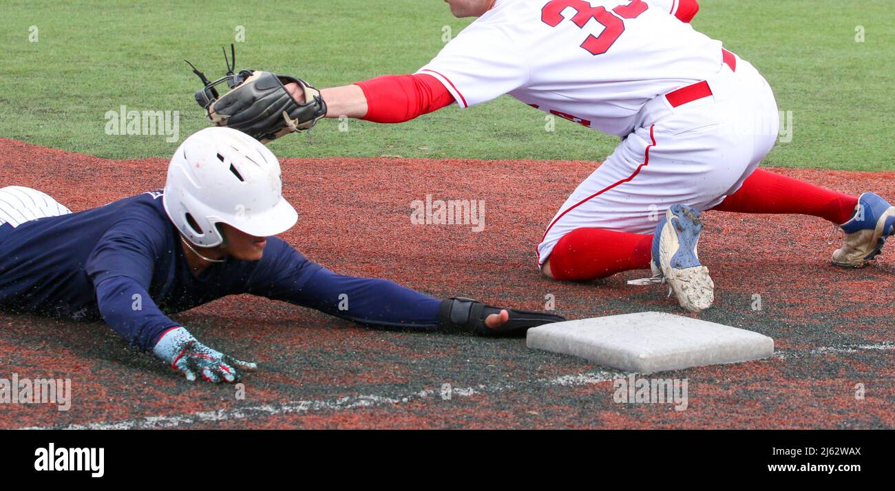 Un joueur de baseball glisse la tête d'abord dans la troisième base en évitant l'étiquette pendant un match de lycée gros plan. Banque D'Images