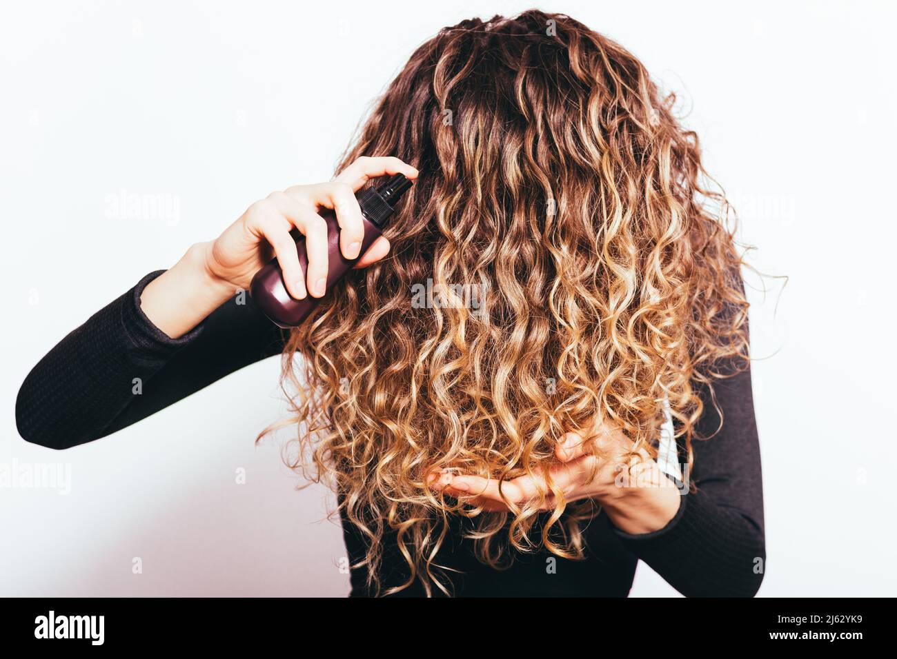 Jeune femme tenant ses cheveux bruns bouclés appliquant de l'huile cosmétique nutritionnelle Banque D'Images