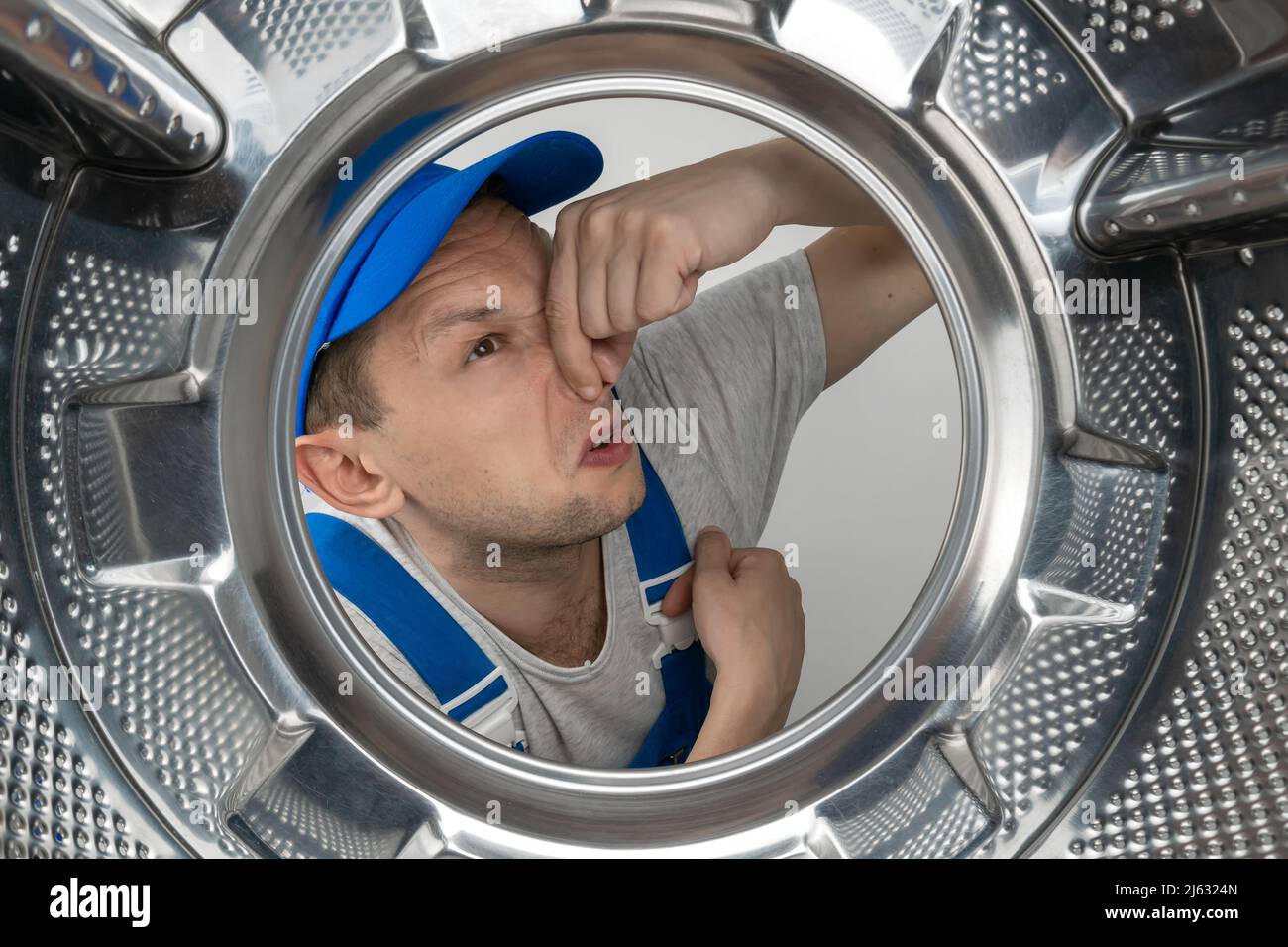 Le réparateur mâle en uniforme regarde dans le tambour d'une machine à laver et couvre son nez d'une odeur désagréable, photo de l'intérieur Banque D'Images