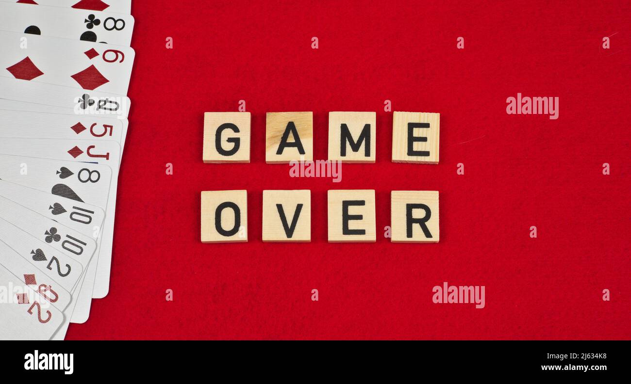 Phrase « Game Over » composée de plaques en bois et de cartes à jouer sur fond de feutre rouge Banque D'Images