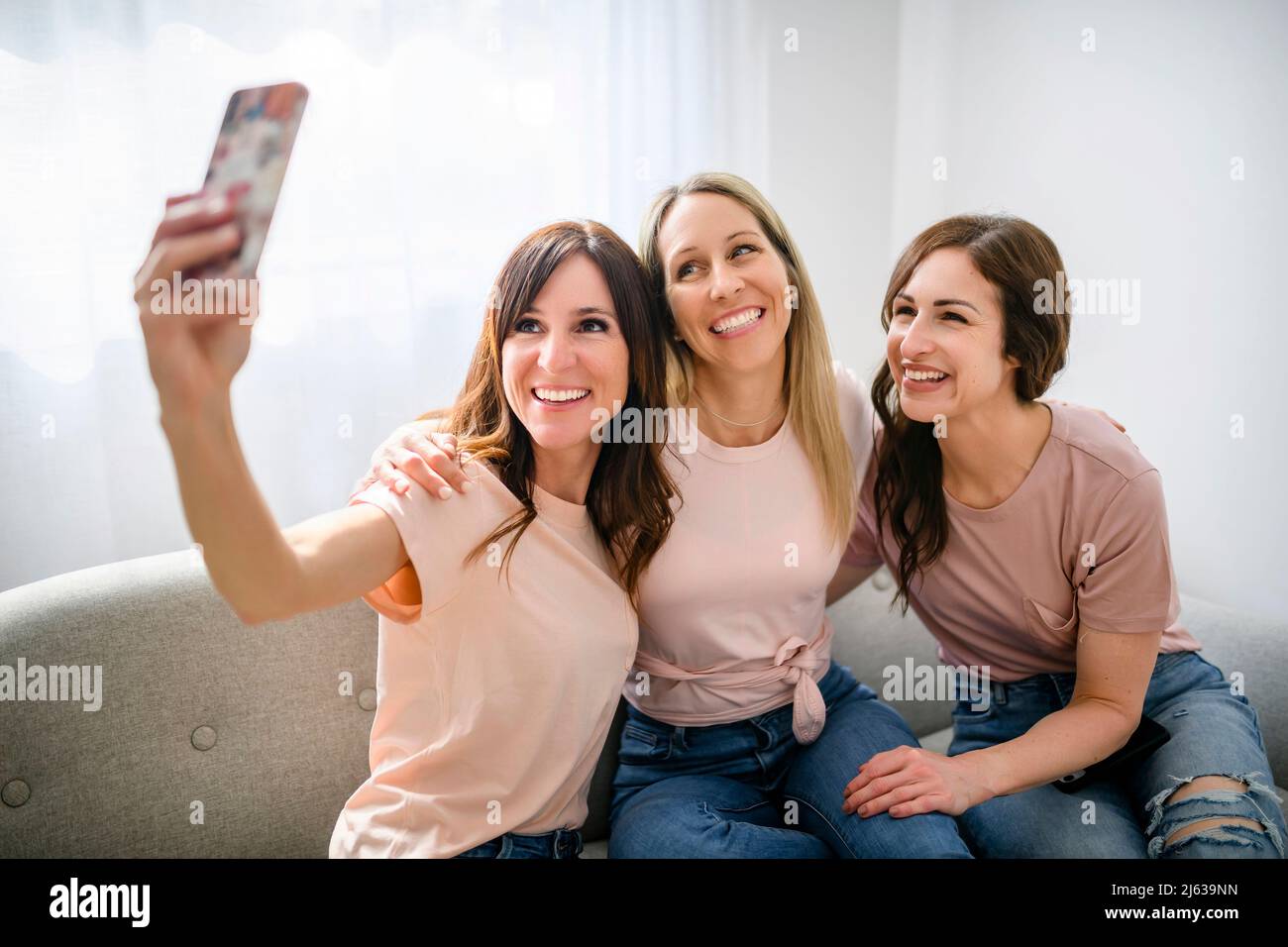 Trois joyeuse femme utilisant un smartphone mobile à la maison assis sur un canapé prendre une photo Banque D'Images