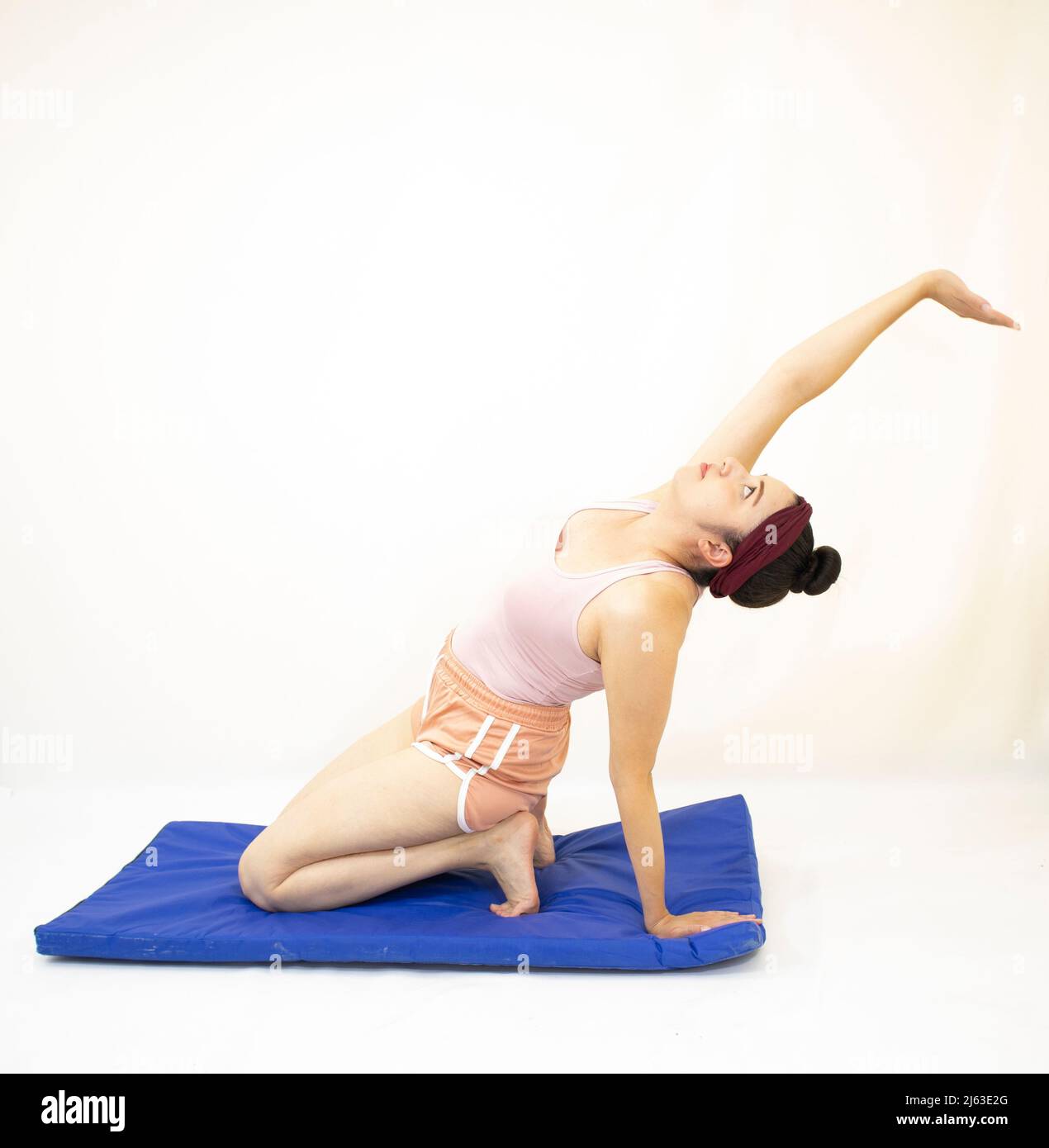 pratiquer le yoga belle femme bras tendu sur le tapis bleu portant des  vêtements de sport roses sur fond blanc Photo Stock - Alamy