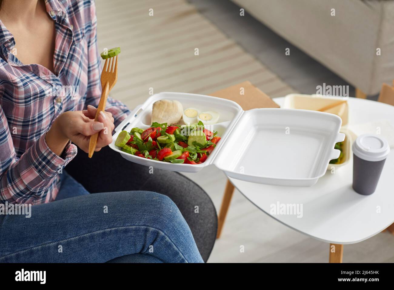 Femme mangeant de délicieux aliments à la maison à partir d'un contenant en plastique du service de livraison de nourriture. Banque D'Images