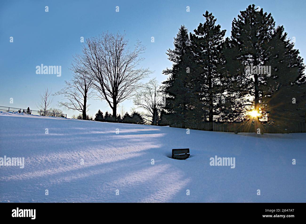 Coucher de soleil sur un parc public avec de la neige profonde couvrant le banc du parc Banque D'Images