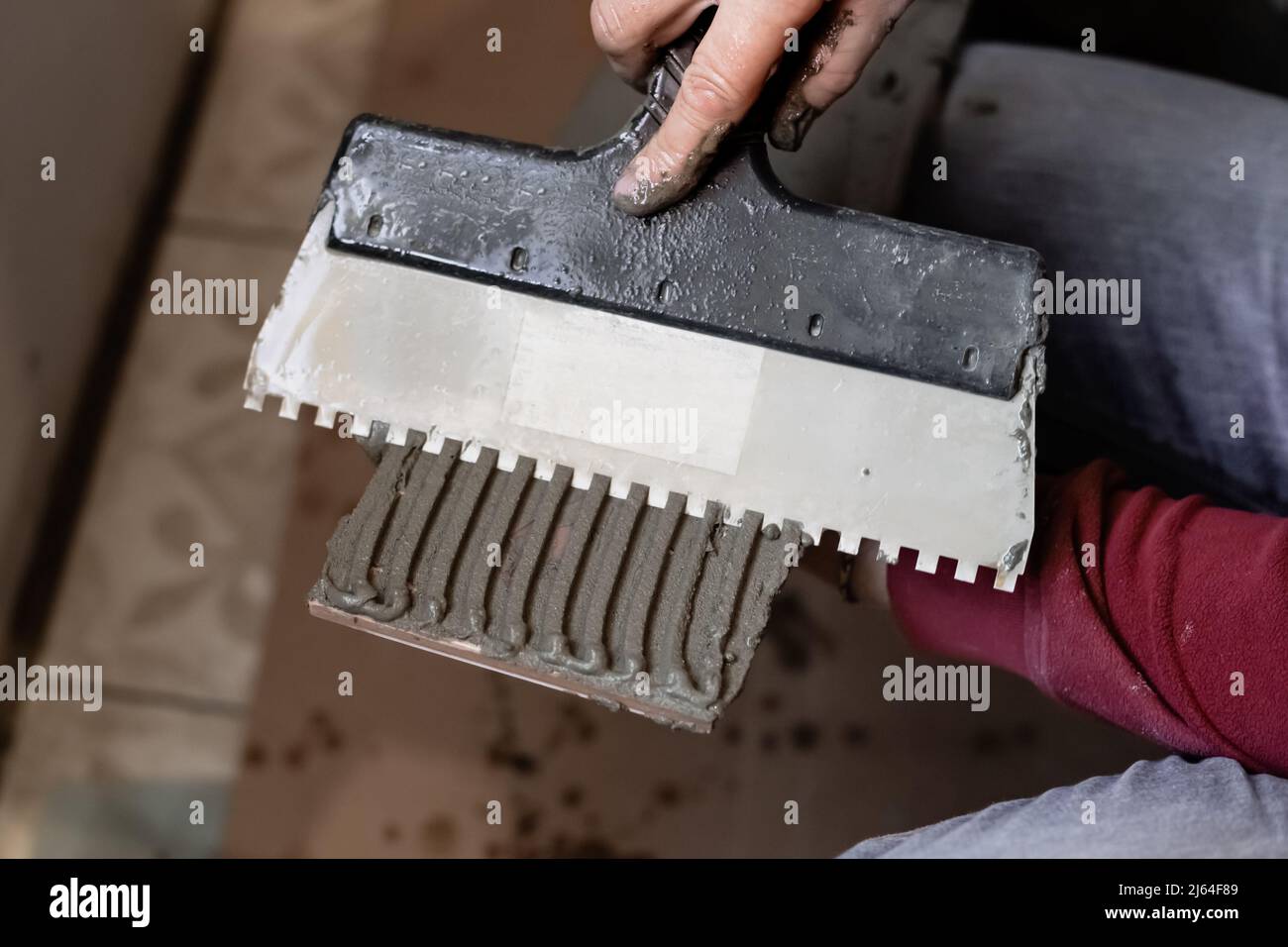 Un homme applique un adhésif pour carreaux avec une truelle sur un carreau. Pose de carreaux sur le mur. Banque D'Images