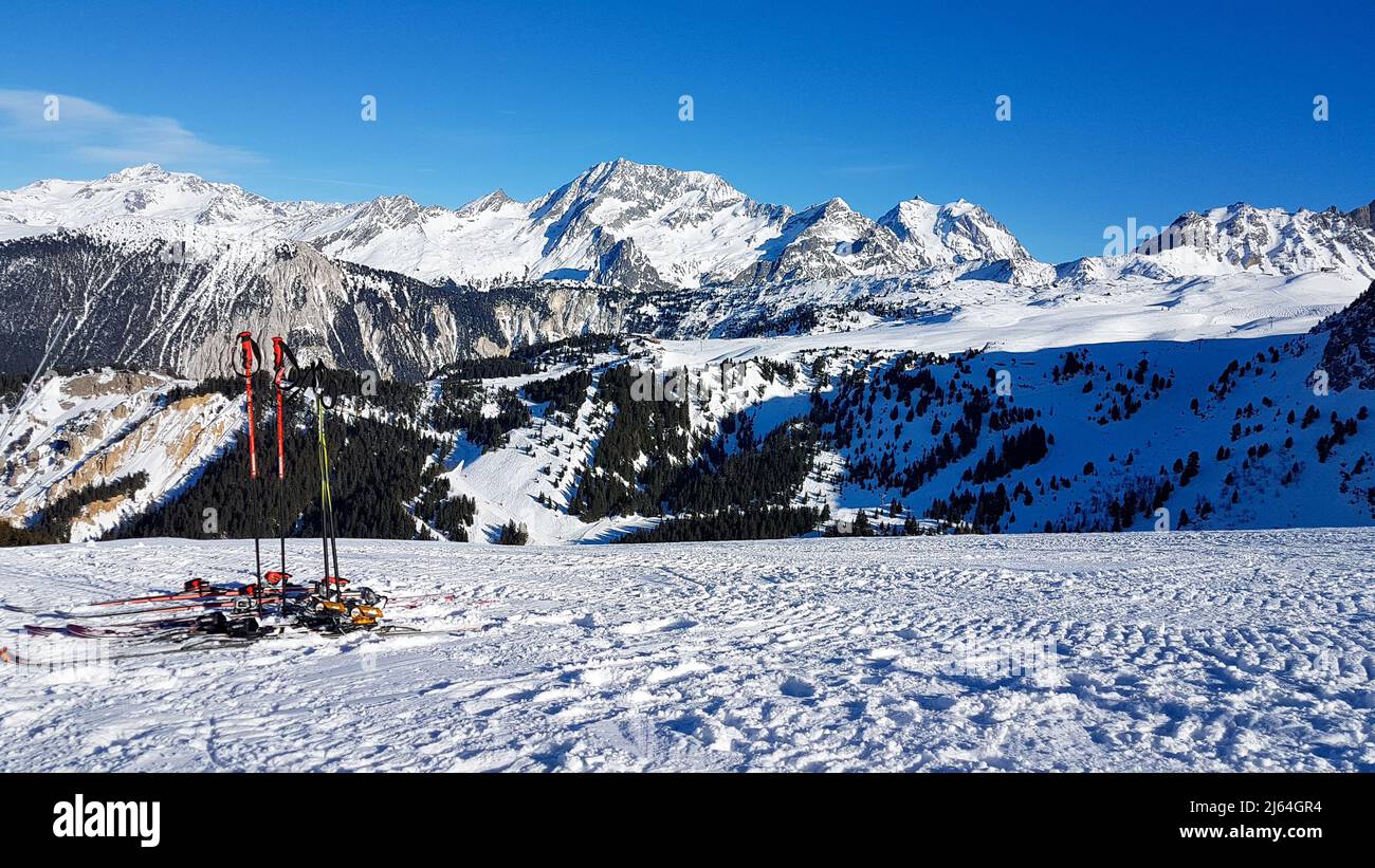 Skis et bâtons debout sur une pente dans les Alpes françaises donnant sur les montagnes blanches sous un ciel bleu clair Banque D'Images