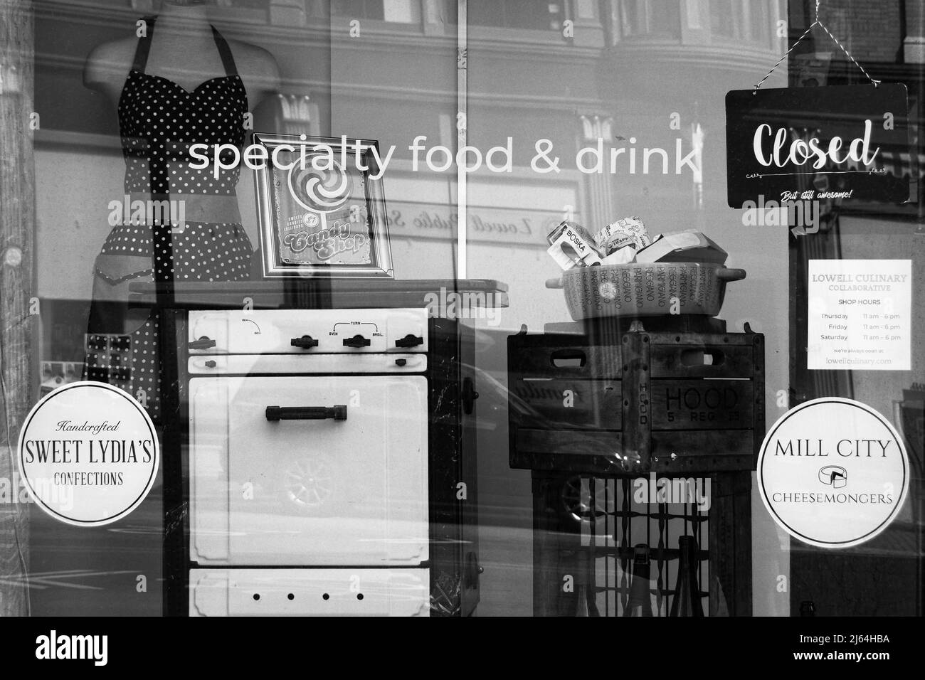 Une vue à travers une fenêtre de la façade d'un magasin d'alimentation spécialisé avec un petit poêle de cuisine d'époque en premier plan et un mannequin d'époque portant un tablier Banque D'Images