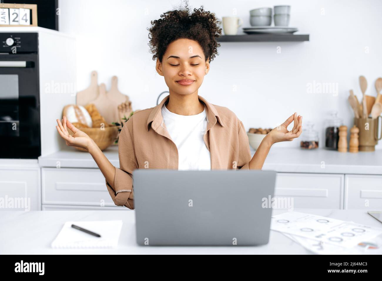 Méditation et relaxation. Bonne fille millénaire afro-américaine, étudiante ou pigiste, assis dans la cuisine à la table, prend une pause de travail ou d'étude, médite, détend le cerveau, souriant Banque D'Images