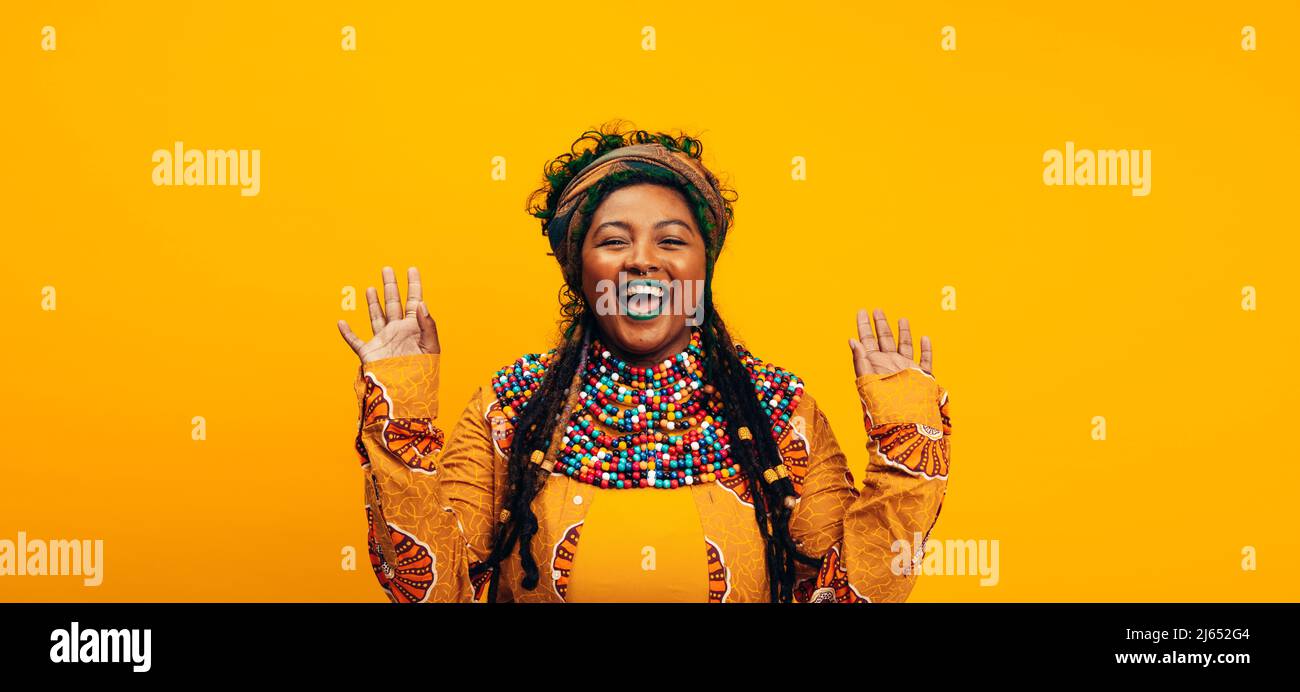 Femme ethnique gaie portant des vêtements traditionnels. Jeune femme à la mode souriant à l'appareil photo tout en se tenant debout sur un fond jaune. Élégant Banque D'Images