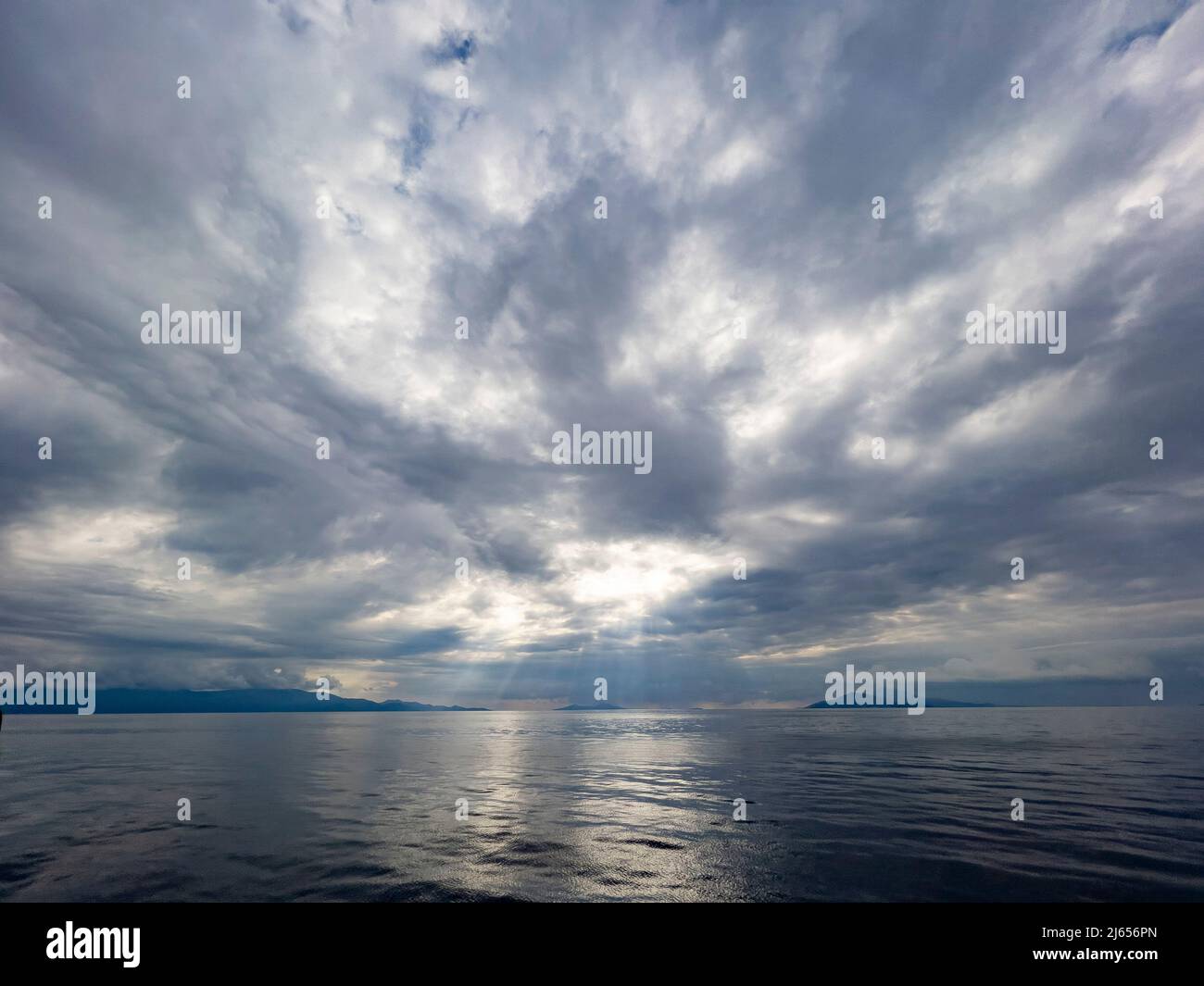 Le silence avant la tempête. Poutres de soleil tombant des nuages gris. Vue sur le ciel et la montagne du point de vue de la mer. Magnifique arrière-plan naturel Banque D'Images