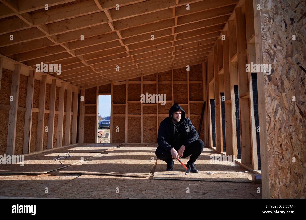 Homme ingénieur bâtiment en bois cadre maison dans la maison de style scandinave. Homme développeur sur le chantier, inspectant la qualité du travail le jour ensoleillé, tenant le marteau en main. Banque D'Images