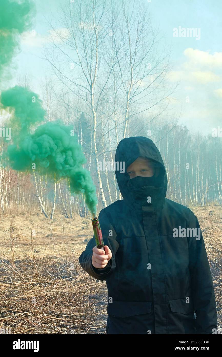 Une préadolescence dans une veste noire et un masque contient la bombe verte de fumée Banque D'Images