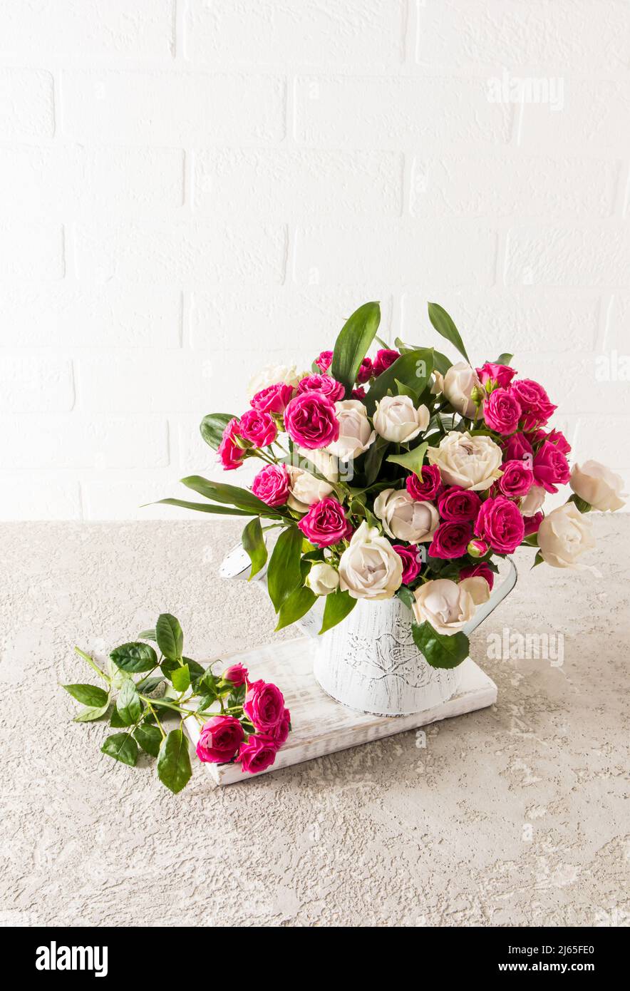 un beau bouquet de roses de jardin frais dans un vase décaratif sous forme d'arrosoir. table en béton contre un mur en brique blanche Banque D'Images