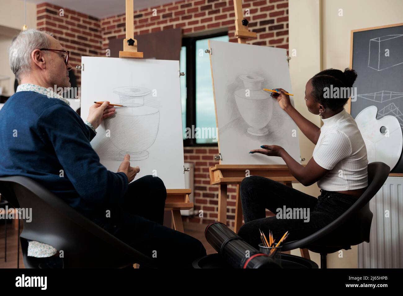 Homme senior enseignant supervisant un jeune étudiant pendant un cours de dessin dans un studio de créativité développant des compétences artistiques. Artiste esquissant un modèle de vase sur toile à l'aide de la technique de dessin. Banque D'Images