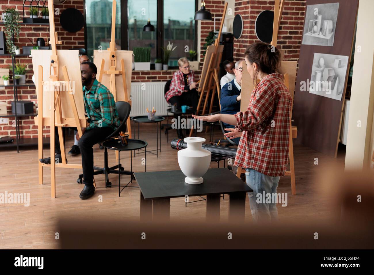 Professeur de peintre montrant le modèle pour le cours de dessin expliquant la technique d'illustration pendant la leçon d'art en studio de créativité. Vase d'esquisse multiethnique d'équipe sur toile de peinture à l'aide d'un crayon graphique Banque D'Images