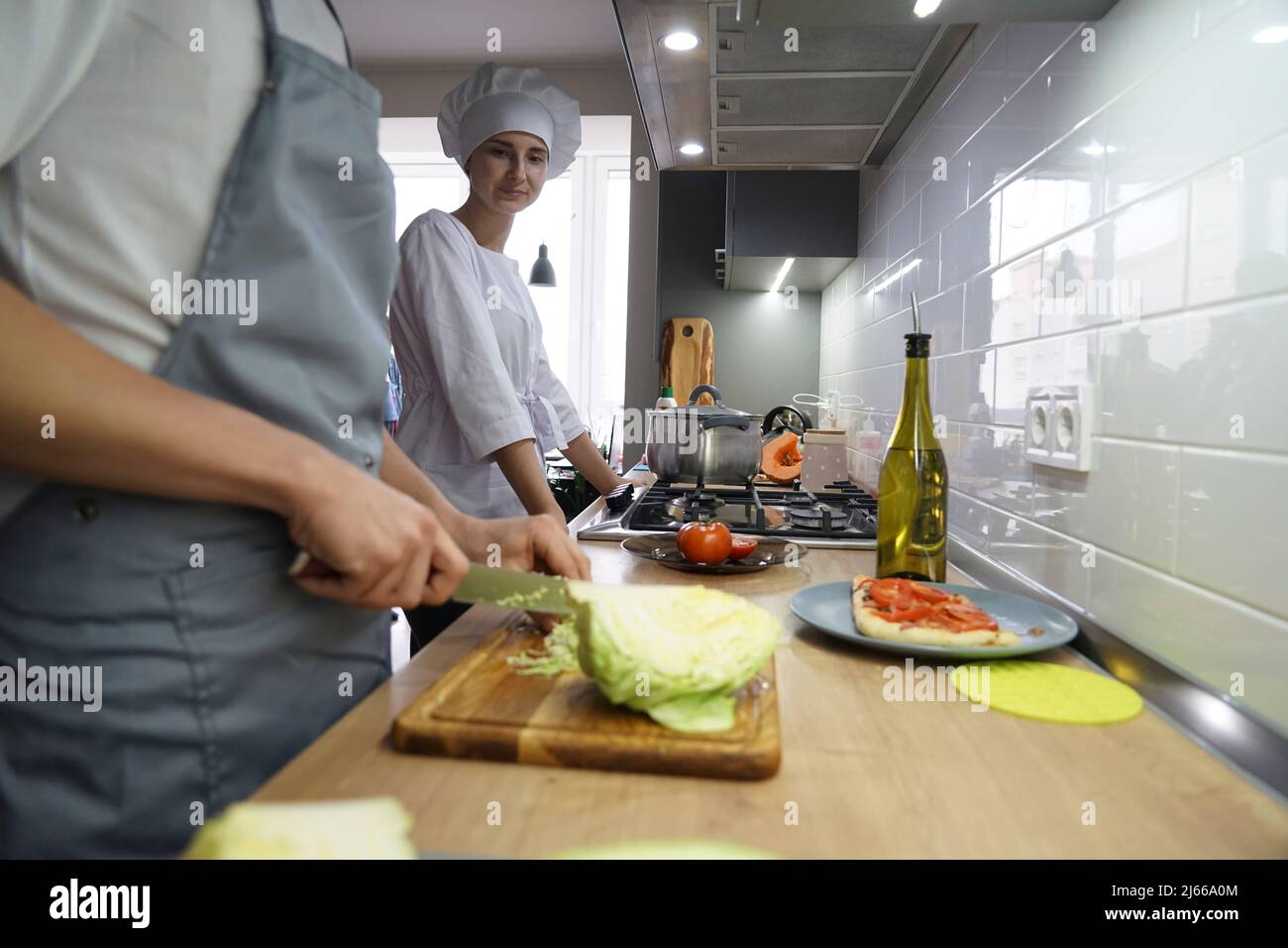Deux chefs dans la cuisine du restaurant préparent la nourriture. Le chef est habillé d'une tunique blanche et d'un chapeau de chef. Banque D'Images