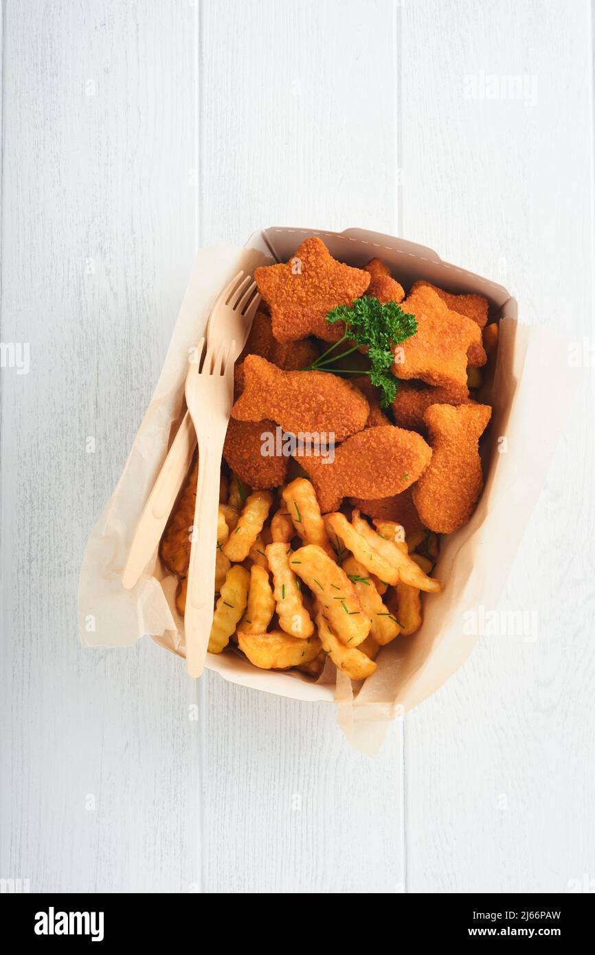 Fish and Chips, restauration rapide britannique. Bâtonnets de poisson avec frites sur une assiette en papier à emporter sur fond en bois blanc. Authentique britannique traditionnel Banque D'Images