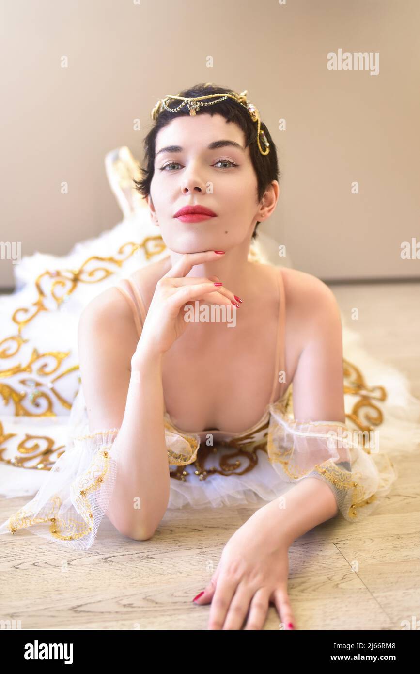 Portrait d'une charmante ballerine couchée sur le sol dans une salle de bal, elle touche son menton avec sa main et regarde avec un air flirtatime à l'appareil photo Banque D'Images
