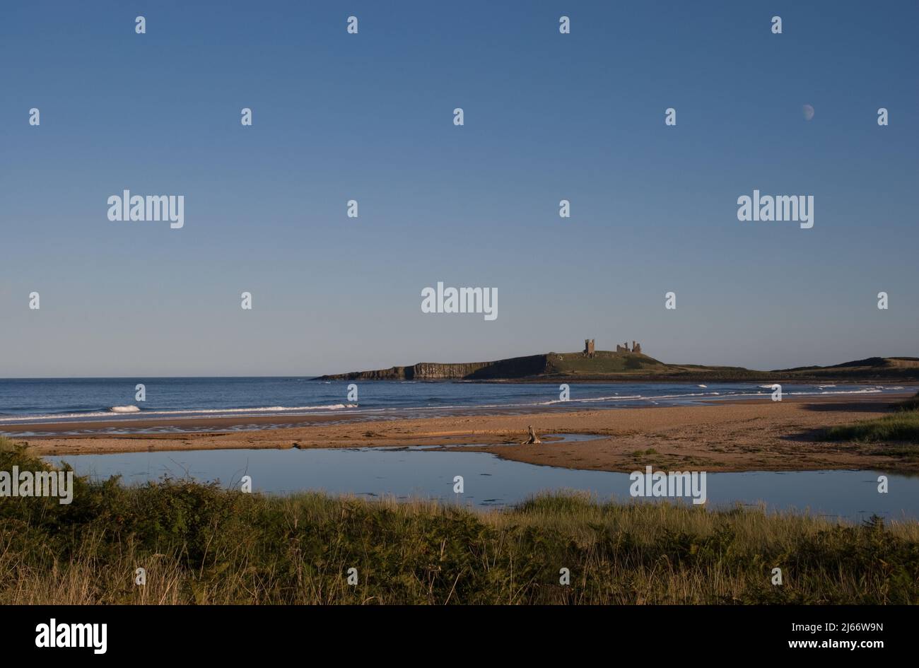 Paysage d'un château de Dunstanburgh éloigné avec lune au-dessus vu au début de la soirée d'automne depuis la plage d'Embleton Banque D'Images