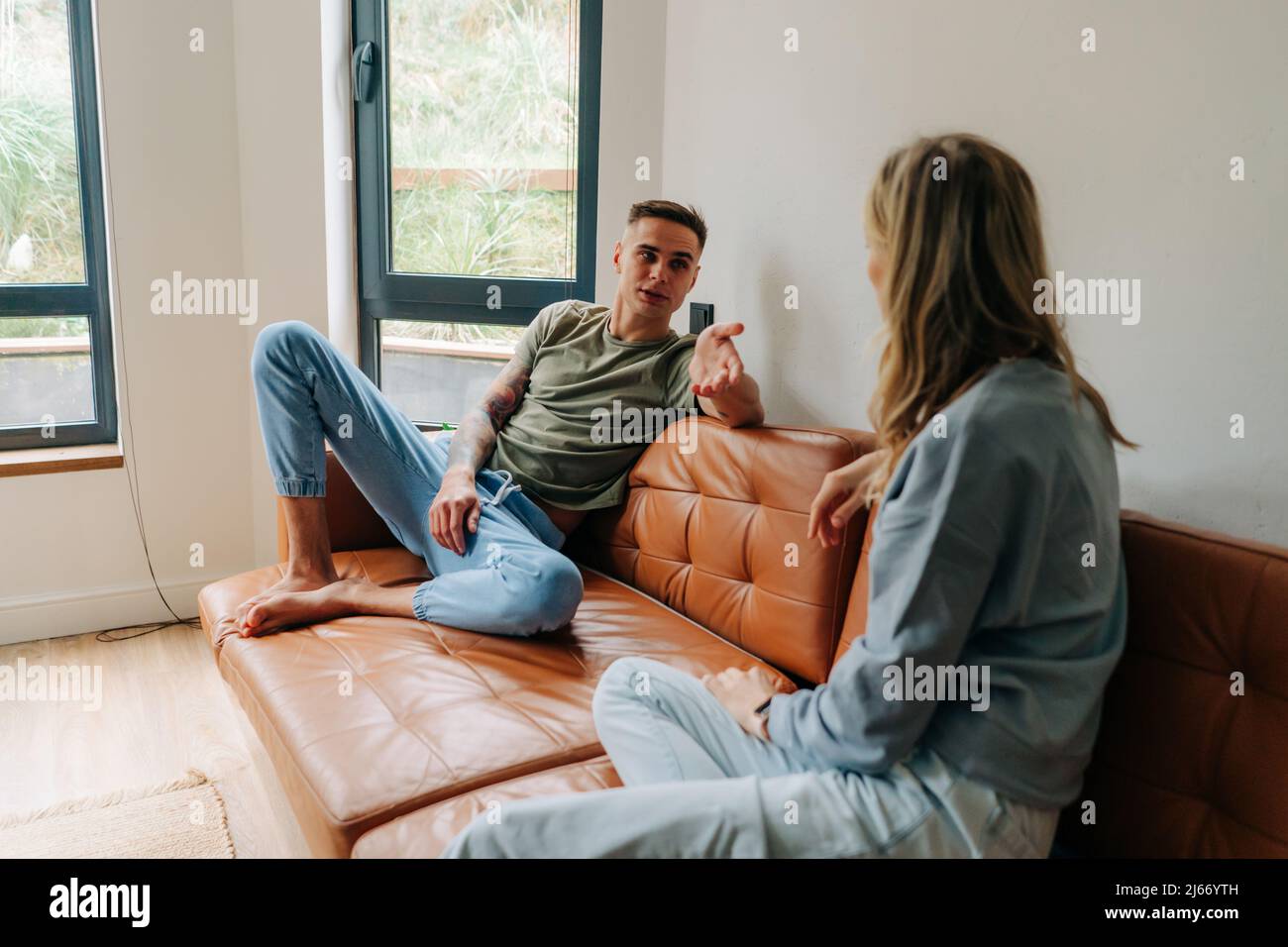 Un jeune homme discute avec sa petite amie en étant assis sur le canapé à la maison, une crise dans les relations familiales. Banque D'Images