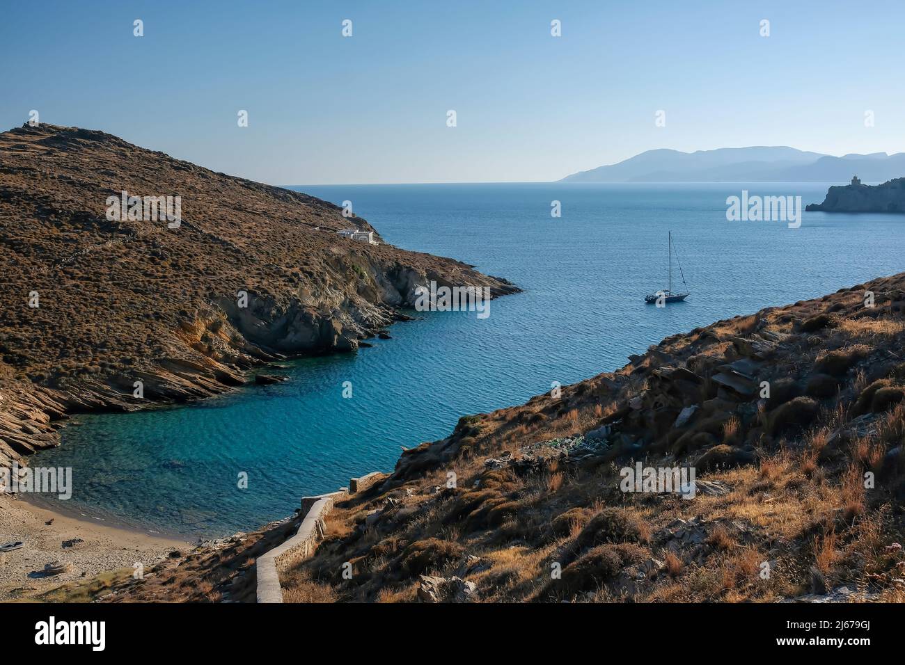 Vue sur la plage de Valmas, un voilier au loin et un phare à l'arrière-plan de l'île d'iOS en Grèce Banque D'Images