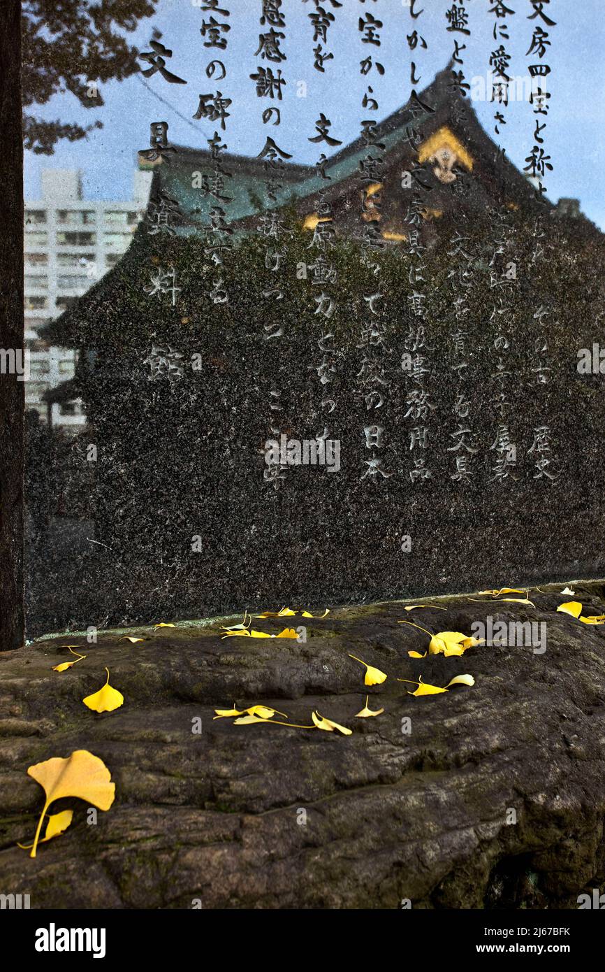 Bâtiment réfléchi sur monument en pierre feuilles ginko d'automne Temple Yushima Tokyo Japon Banque D'Images