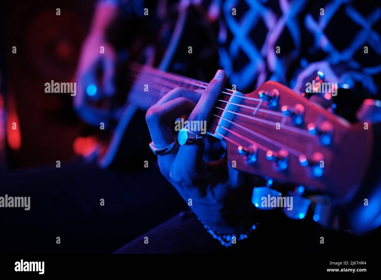 Gros plan moyen d'un jeune musicien masculin méconnaissable jouant de la guitare acoustique à la lumière du néon Banque D'Images