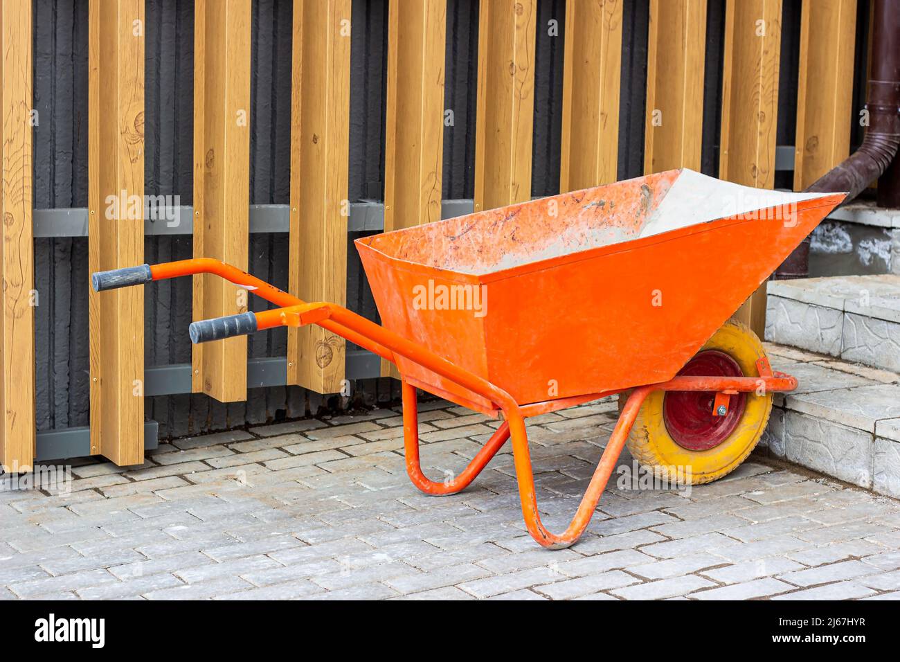 Chariot de brouette orange vif pour le jardinage et le chantier de construction sur la rue. Banque D'Images