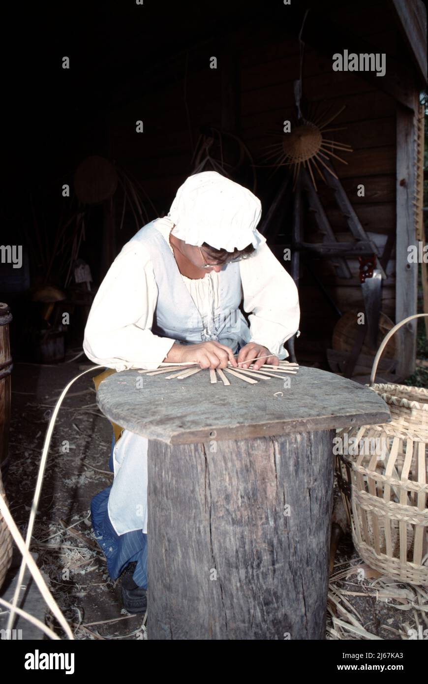 Williamsburg, Virginie. ÉTATS-UNIS 9/1987. Tisserand. Master basket tisserand utilisant des bandes de bois tissées dans un panier de plusieurs tailles pour transporter ou stocker des légumes, des épis de maïs, des fruits, des oeufs, des instruments de couture, bois de chauffage de cuisine, bois de chauffage de cheminée et chiffons à linge. Le tissage du panier est vieux de 1000s ans. Banque D'Images