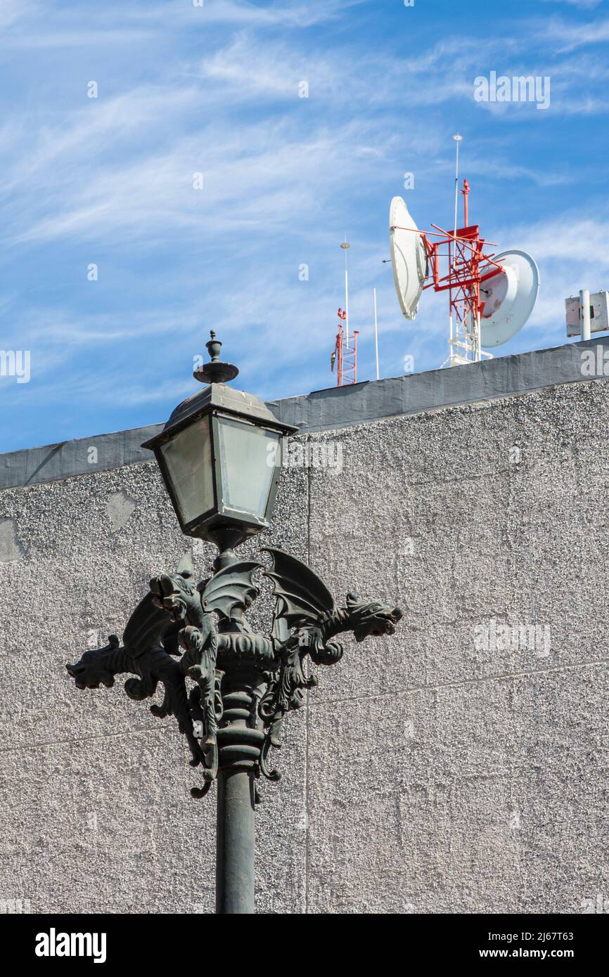 Ancienne lampe orante en fer décorée de dragons stylisés volant dans une rue de Mazatlan, au Mexique, avec un équipement moderne (peut-être radio) sur un toit Banque D'Images