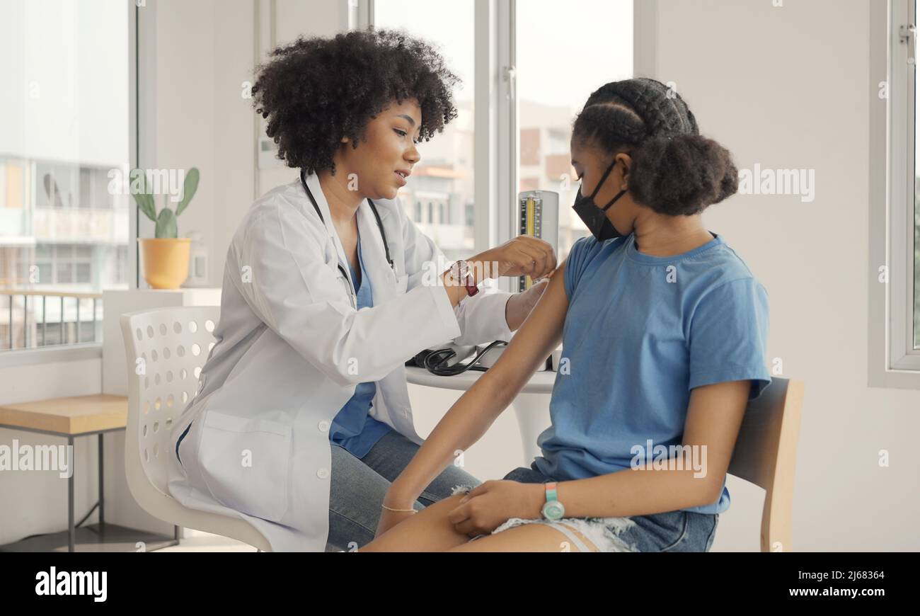 Un médecin afro-américain applique du plâtre sur l'épaule d'un enfant après avoir été vacciné. Ouverture des manches pour vacciner contre la grippe ou l'épidémie dans la guérison Banque D'Images